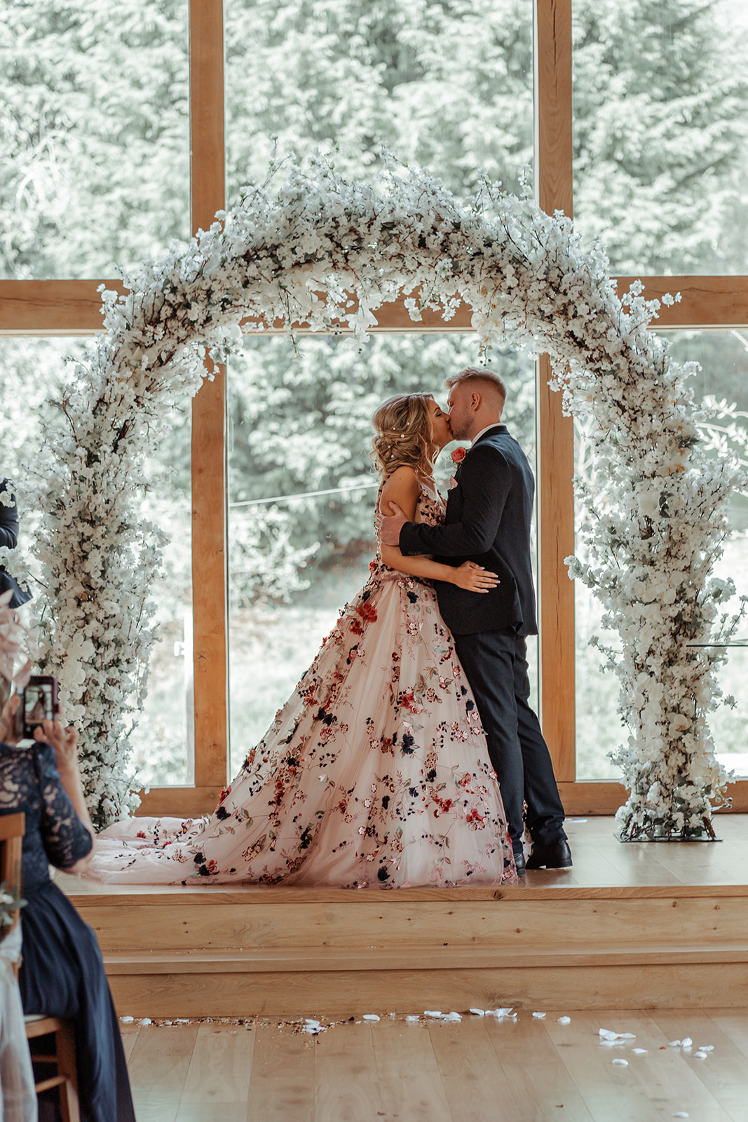 Ronald Joyce real bride, Rebecca, and her husband, Michael, kissing after saying their vows. Rebecca has curled blonde hair and wears our blush Celestina ballgown wedding dress with claret, navy and green floral appliques.